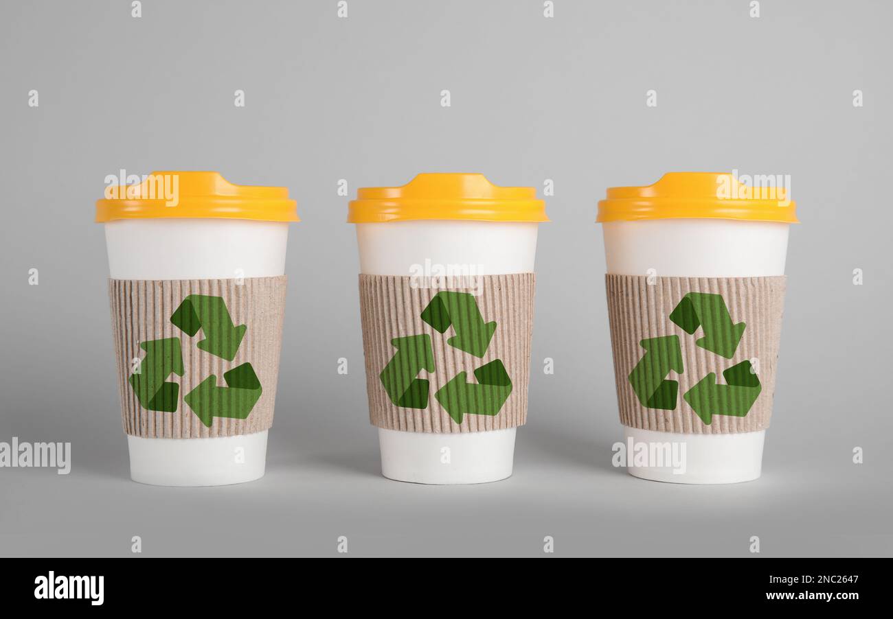 Carton cups with recycling symbols on grey background Stock Photo