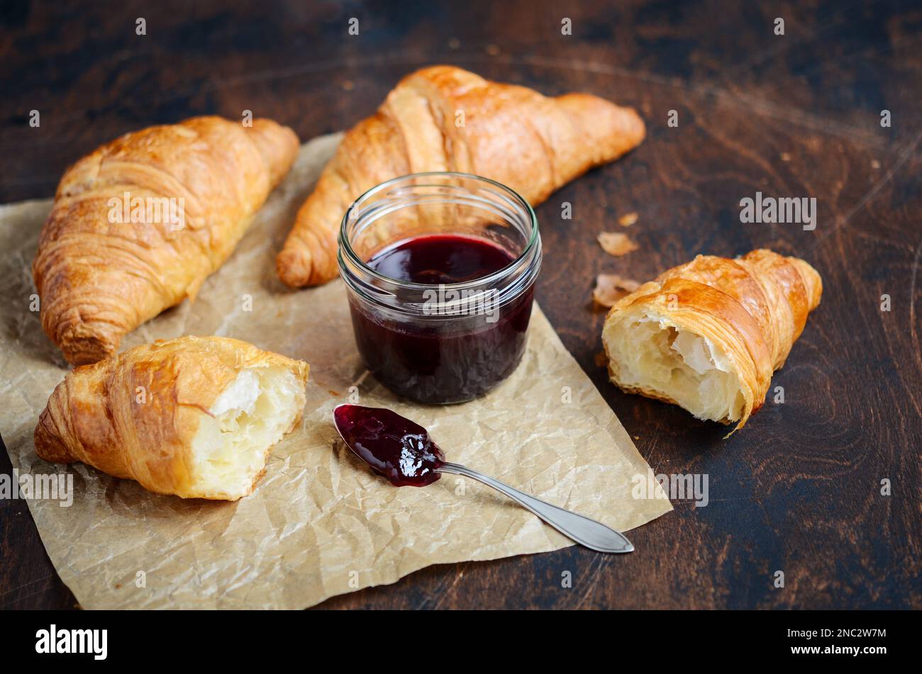 Freshly baked croissants with jam on dark wooden background. Stock Photo