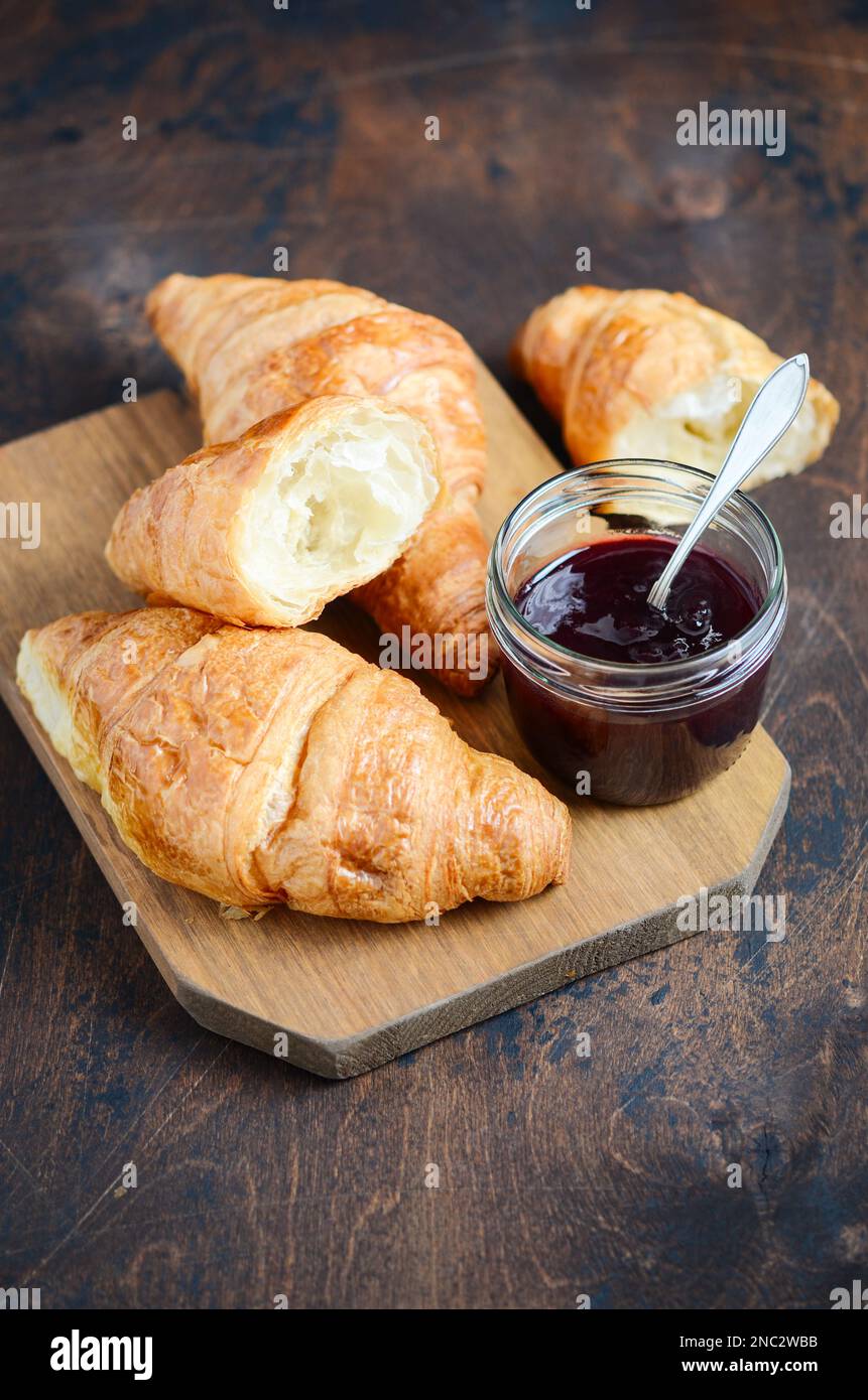 Freshly baked croissants with jam on dark wooden background. Stock Photo