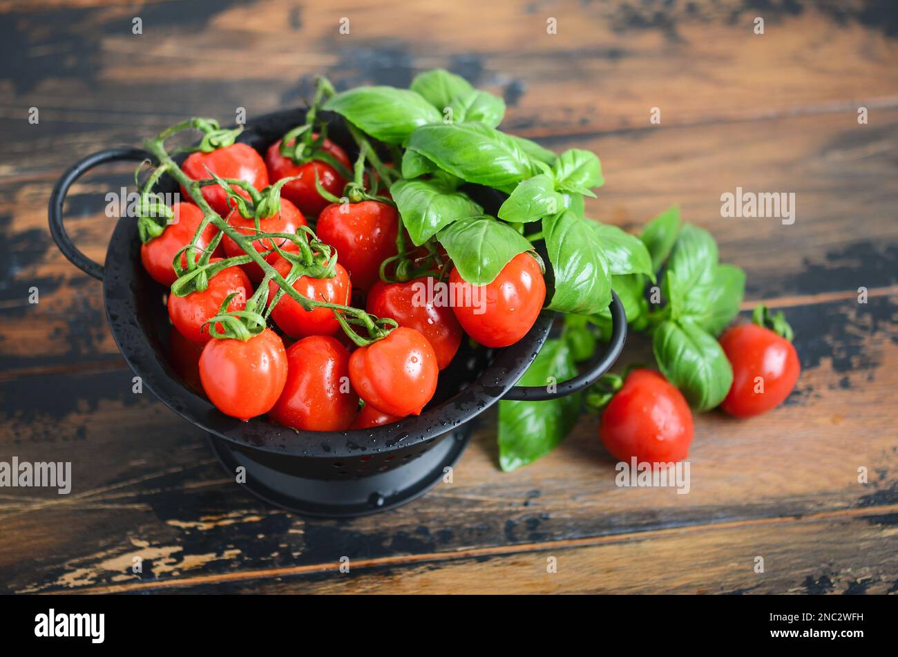 Fresh red cherry tomatoes with basil on a wooden background. Stock Photo