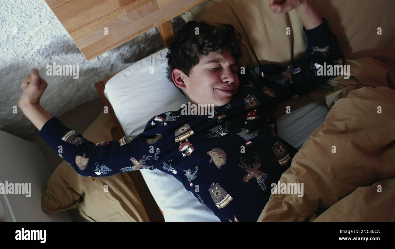 One young boy laying in bed yawning in the morning. Kid waking up rubbing face and eyes