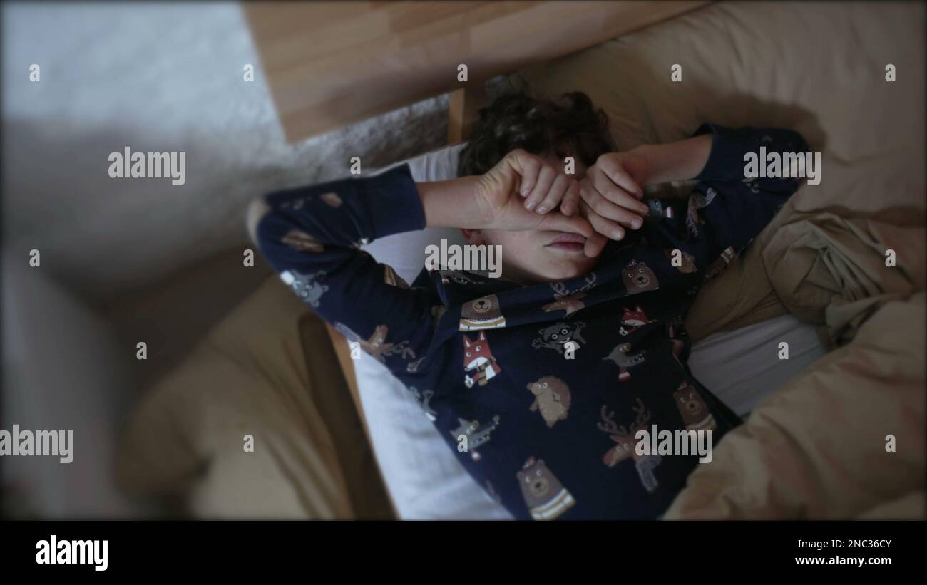 Preteen kid rubbing face and eyes laying in bed. Tired Young boy waking
