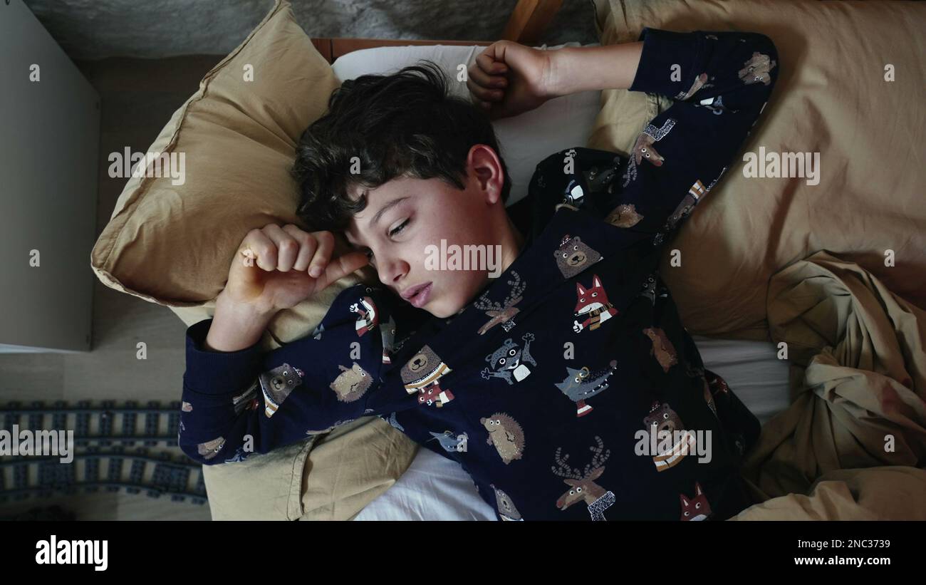 Preteen kid rubbing face and eyes laying in bed. Tired Young boy waking