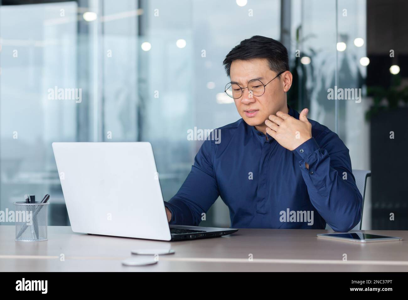 Worried and tired young Asian man working in office on laptop. He feels