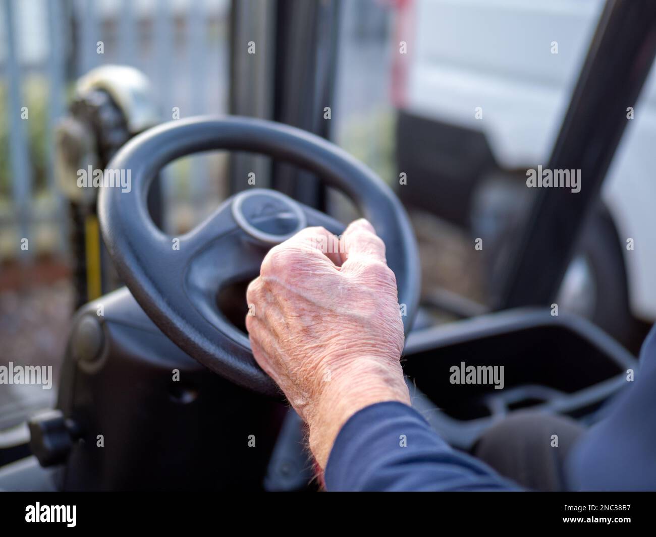 Older mans hands on the steering wheel of a fork lift truck in the work place back to work after 70 years old Stock Photo