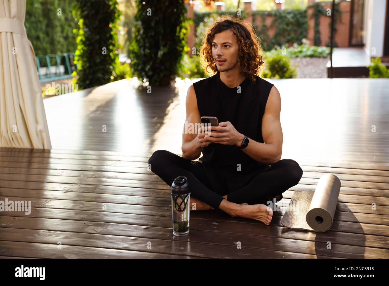 Young ginger man using mobile phone during yoga practice outdoors Stock Photo