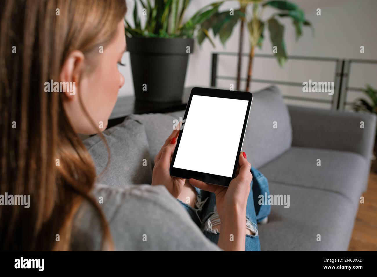 Close-up Unrecognizable Casual blonde young woman in a modern living room lying on a cozy sofa at home, working with blank screen tablet mock-up Stock Photo