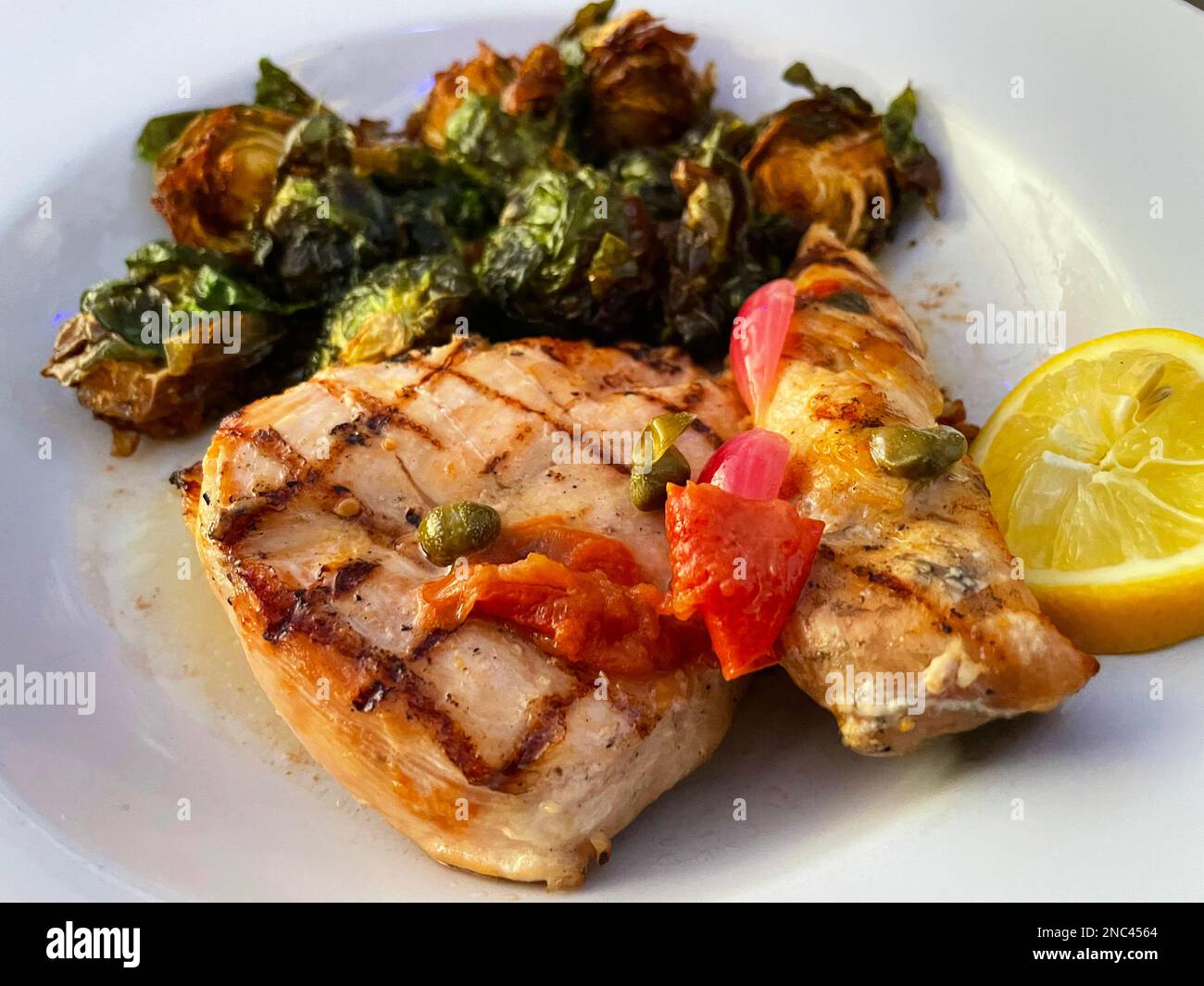 Close-up of grilled chicken with raosted brussel sprouts, lemon, and capers. Stock Photo