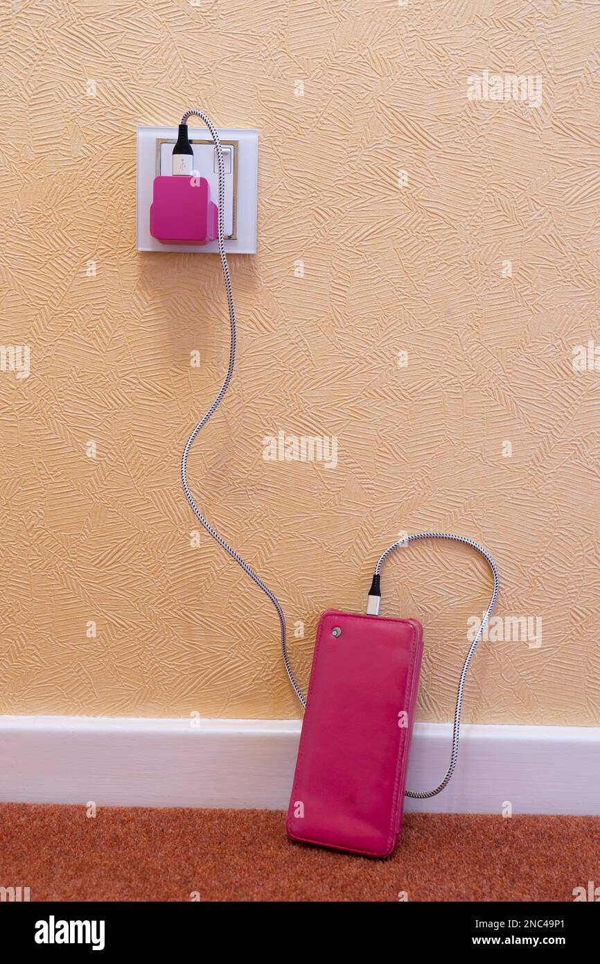 Mobile phone on a floor with a pink case plugged in & charging with a pink USB plug & a cable. Concept: women and technology, feminine phone accessory Stock Photo