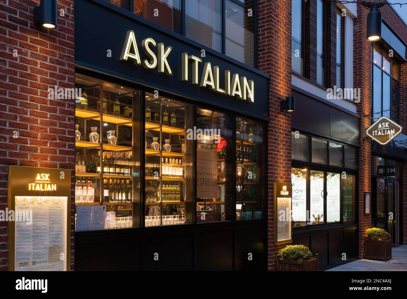 The exterior of Ask Italian restaurant lit up at night with wine bottles in the windows and a menu on the wall. Bell Court, Stratford upon Avon, UK Stock Photo