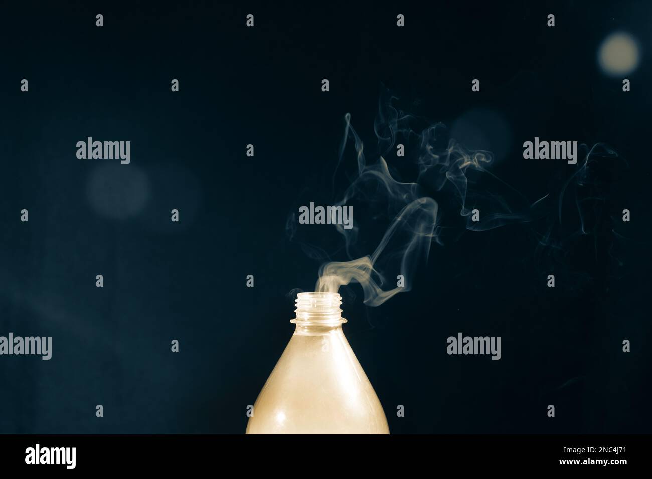 Smoke coming out of a plastic bottle against a black background with flare. Design element. Stock Photo