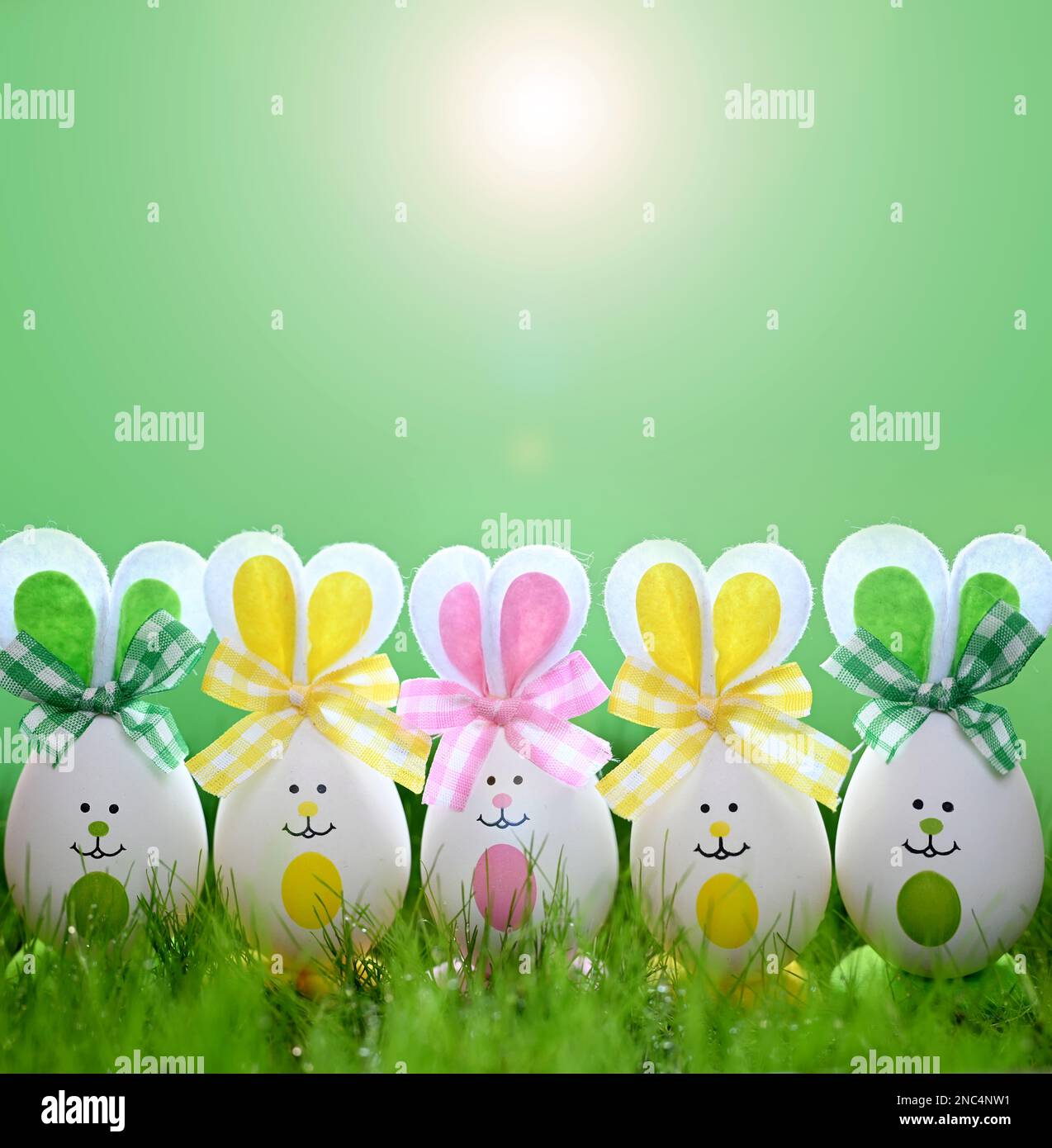 Funny easter eggs in the grass on green background. Happy Easter background. Easter compositions with cute rabbits eggs. Stock Photo