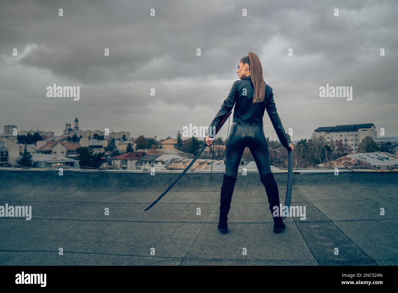 A back view of cool female ninja warrior in leather outfit wielding two Japanese swords Stock Photo