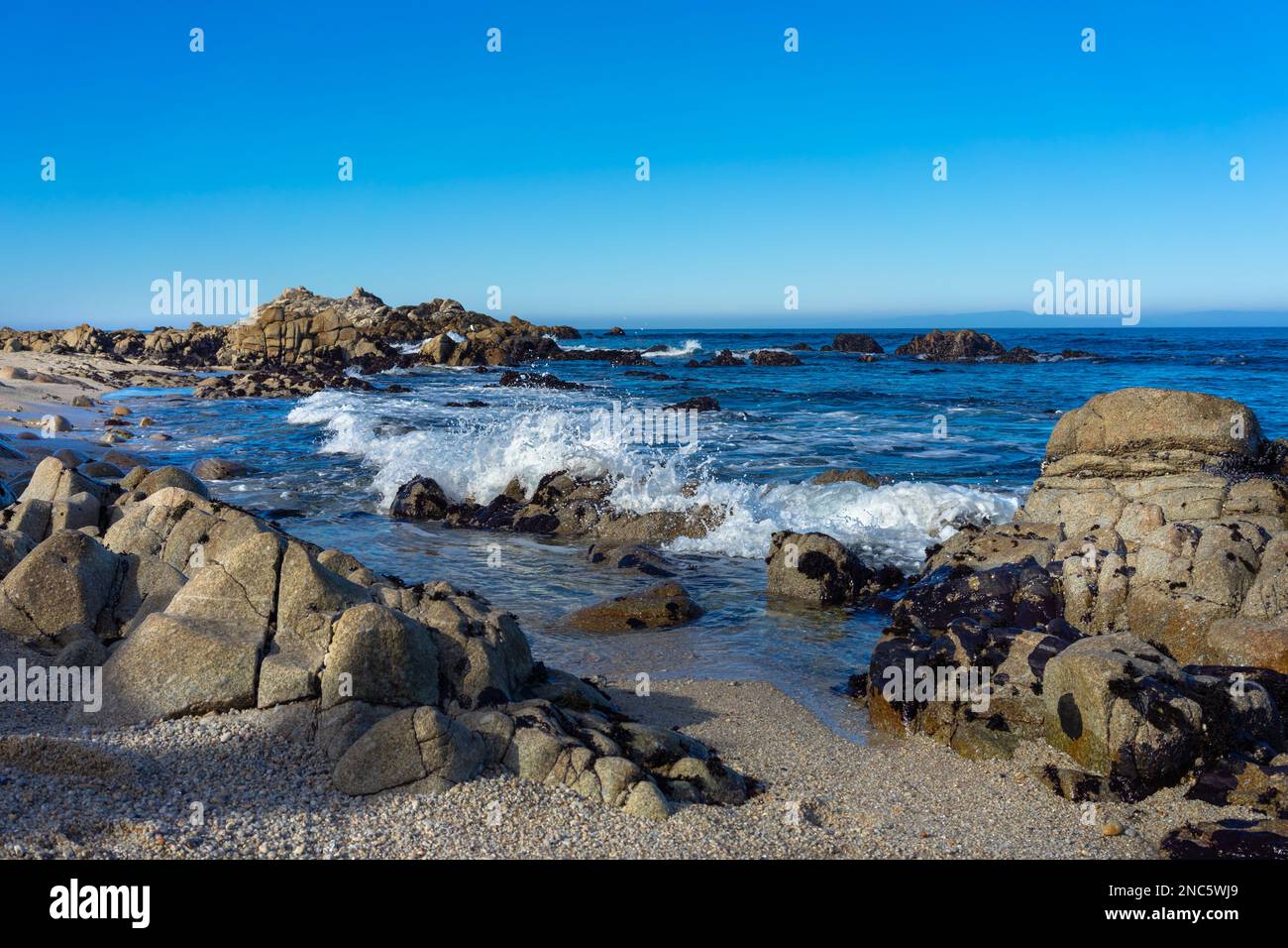 Beach with rock formations and crashing ocean wave at Monterey Bay Stock Photo