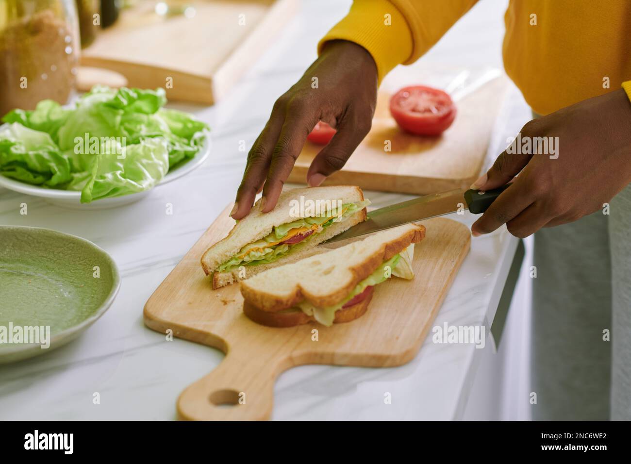 Woman cutting cheese and veggies sandwich in two triangles Stock Photo