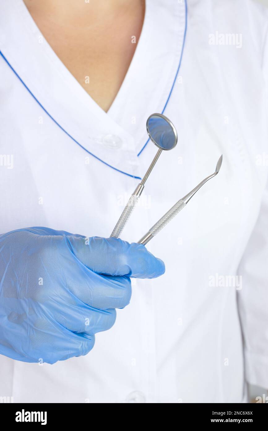 Cropped view of dentist in latex glove holding Dentist Professional tool near dental set blurred on of doctors coat uniform background Stock Photo