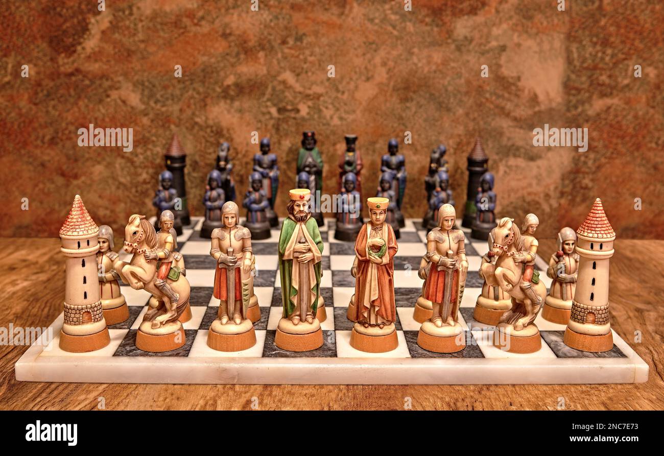White Medieval or Middle Ages chess pieces on a white marble chess board. With the black pieces in the out of focus background. Stock Photo