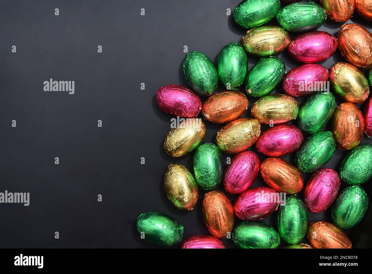 Foil wrapped multi coloured easter eggs in pink, green, orange and yelow in a pile or group, against a grey black background. Stock Photo
