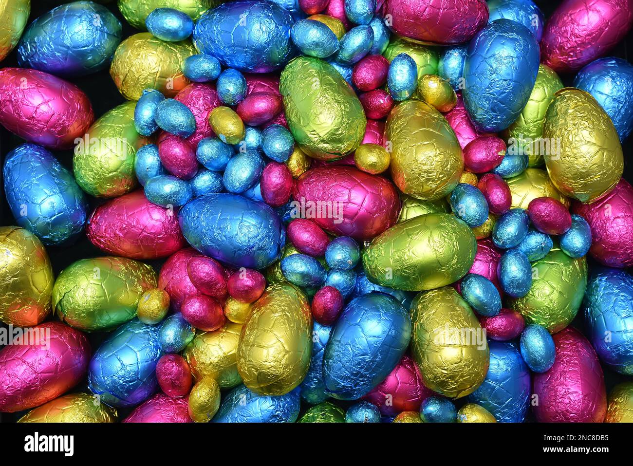 Pile or group of multi colored and different sizes of colourful foil wrapped chocolate easter eggs in pink, blue, yellow and lime green. Stock Photo