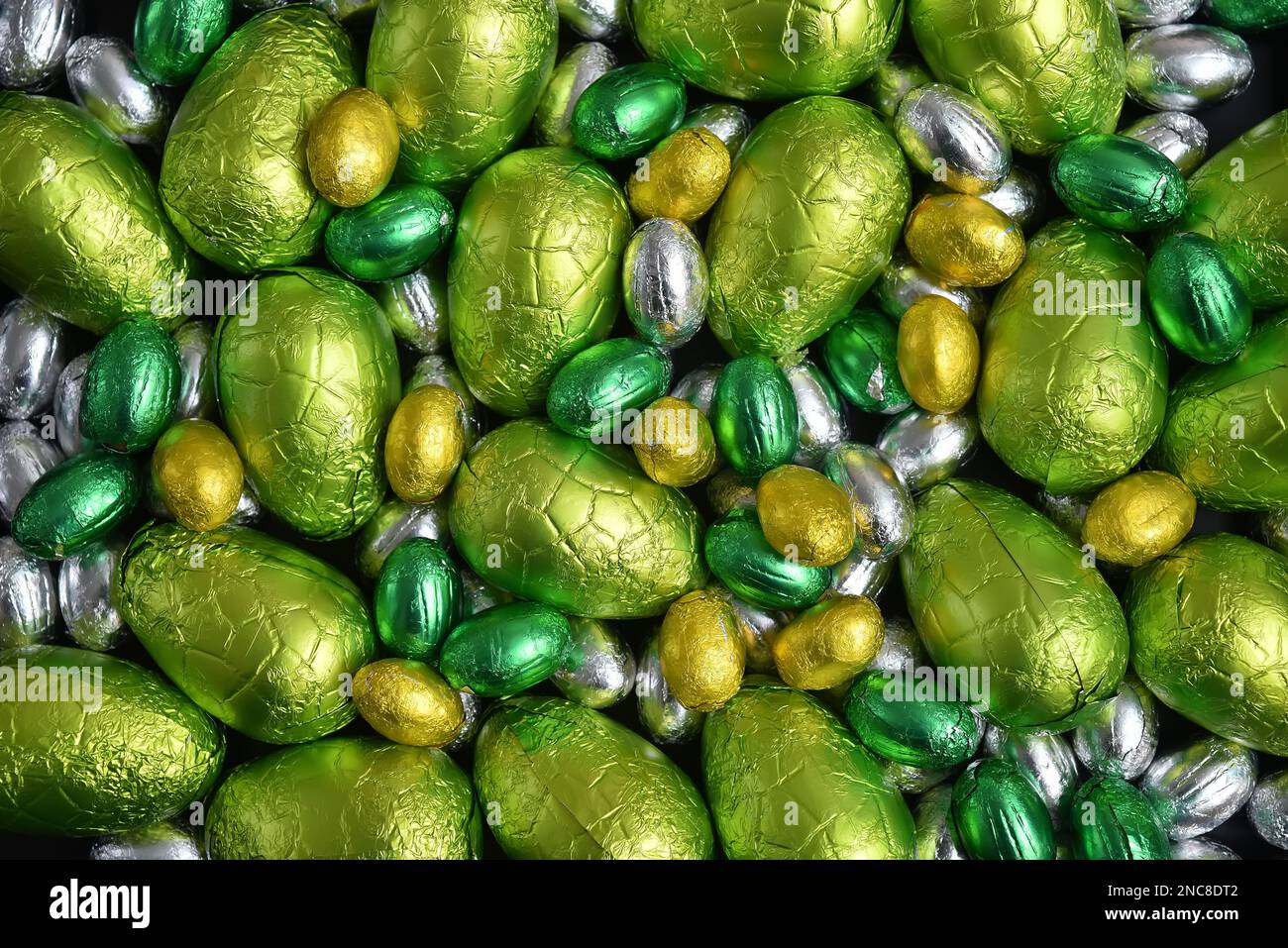 Large & small yellow, gold, green, lime green and silver spring colours of foil wrapped chocolate easter eggs, against a black background. Stock Photo