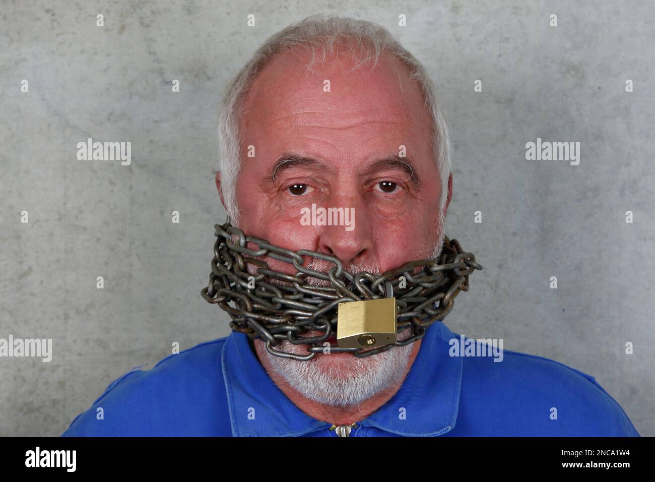 Autocracy, the end of free speech. Portrait of a man in front of a cold concrete wall with his mouth locked with a steel chain. Stock Photo