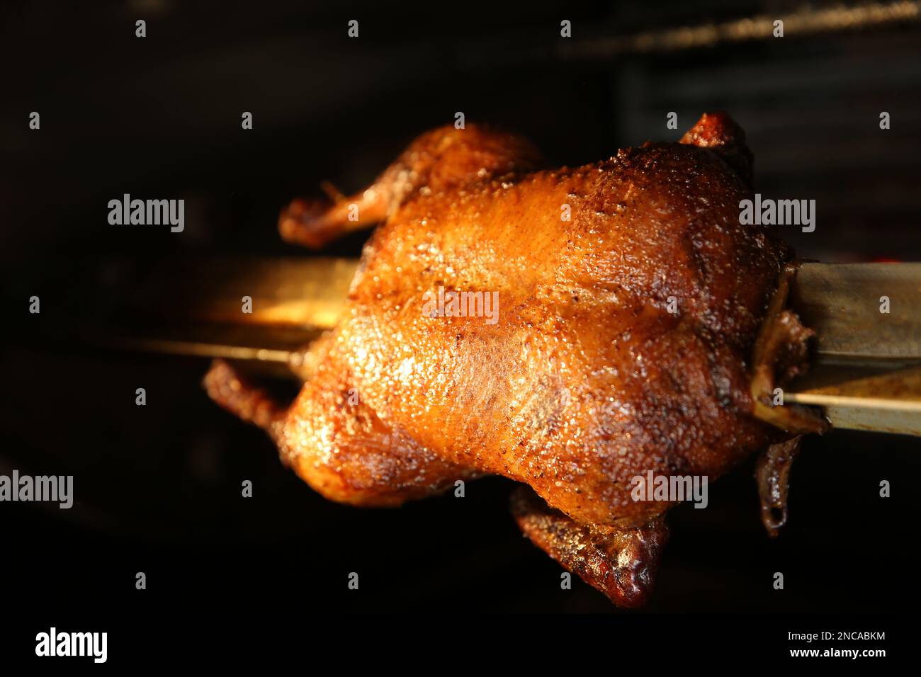 Grilling whole delicious duck in rotisserie machine, closeup Stock