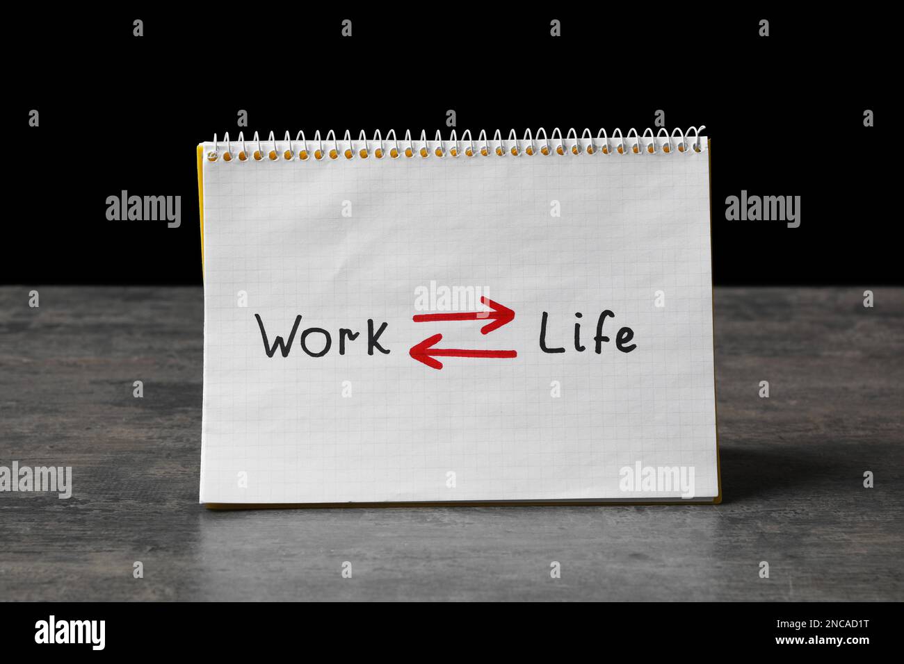 Notebook with words Work, Life and arrows on grey table against black ...