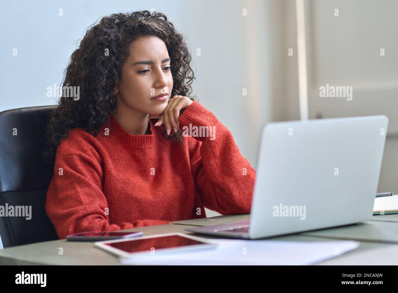 Young latin business woman working on laptop thinking analyzing online data. Stock Photo