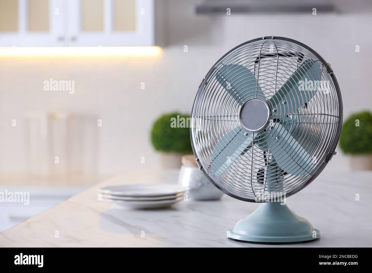 Modern electric fan on countertop in kitchen, space for text. Summer
