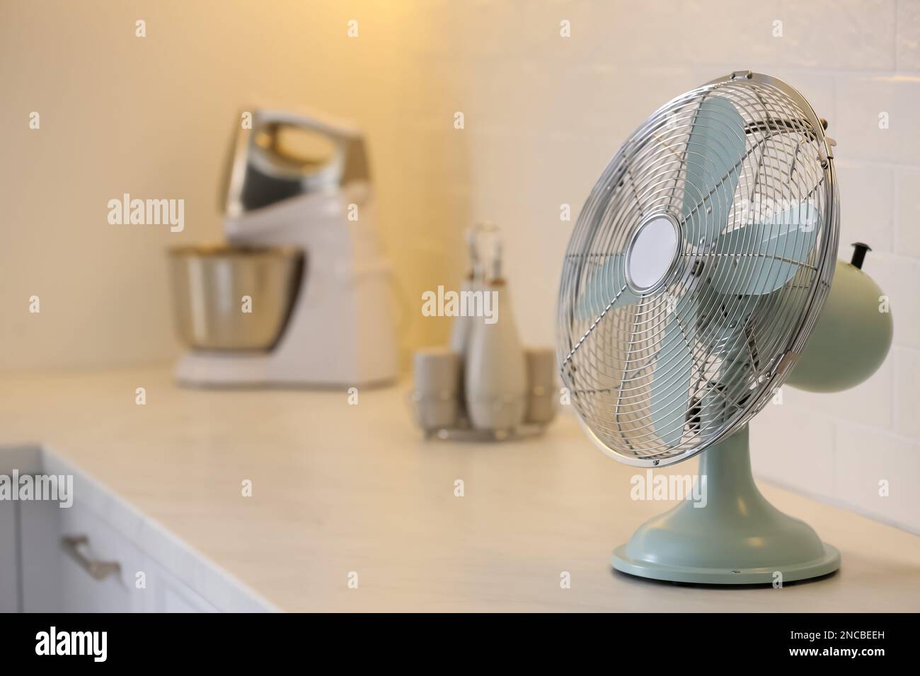 Modern electric fan on countertop in kitchen, space for text. Summer