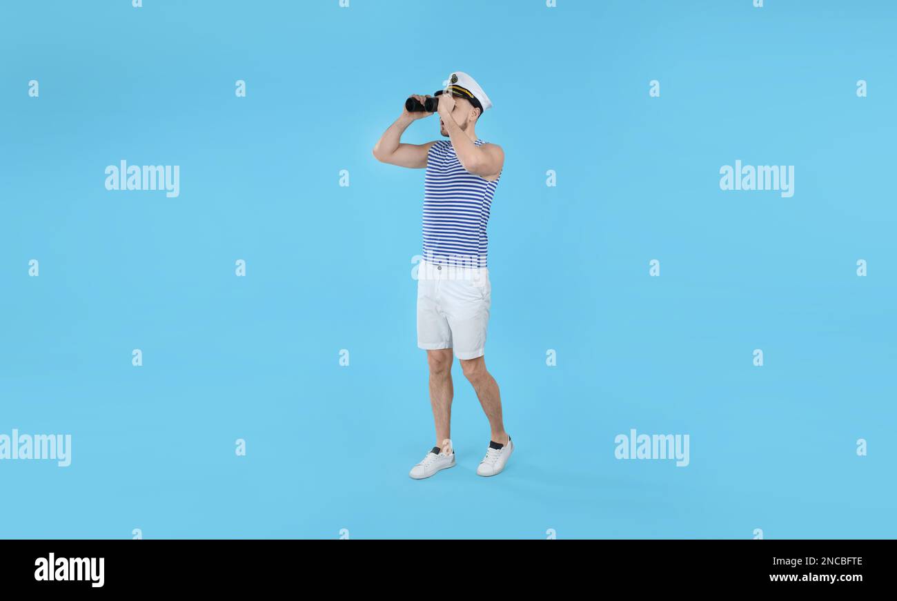 Sailor looking through binoculars on light blue background Stock Photo