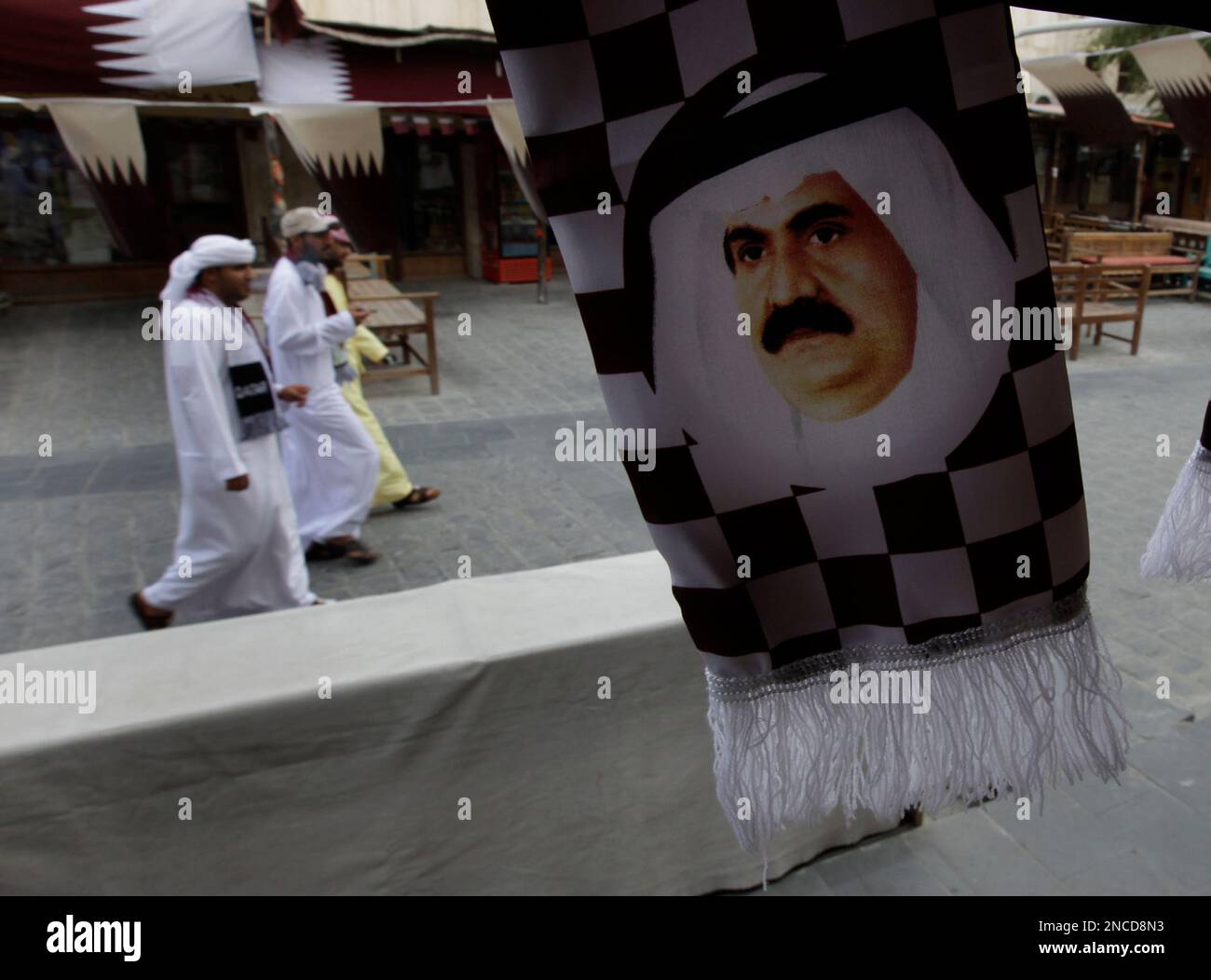 Qatari citizens, left, walk next to a portrait of Qatar's Emir Sheik