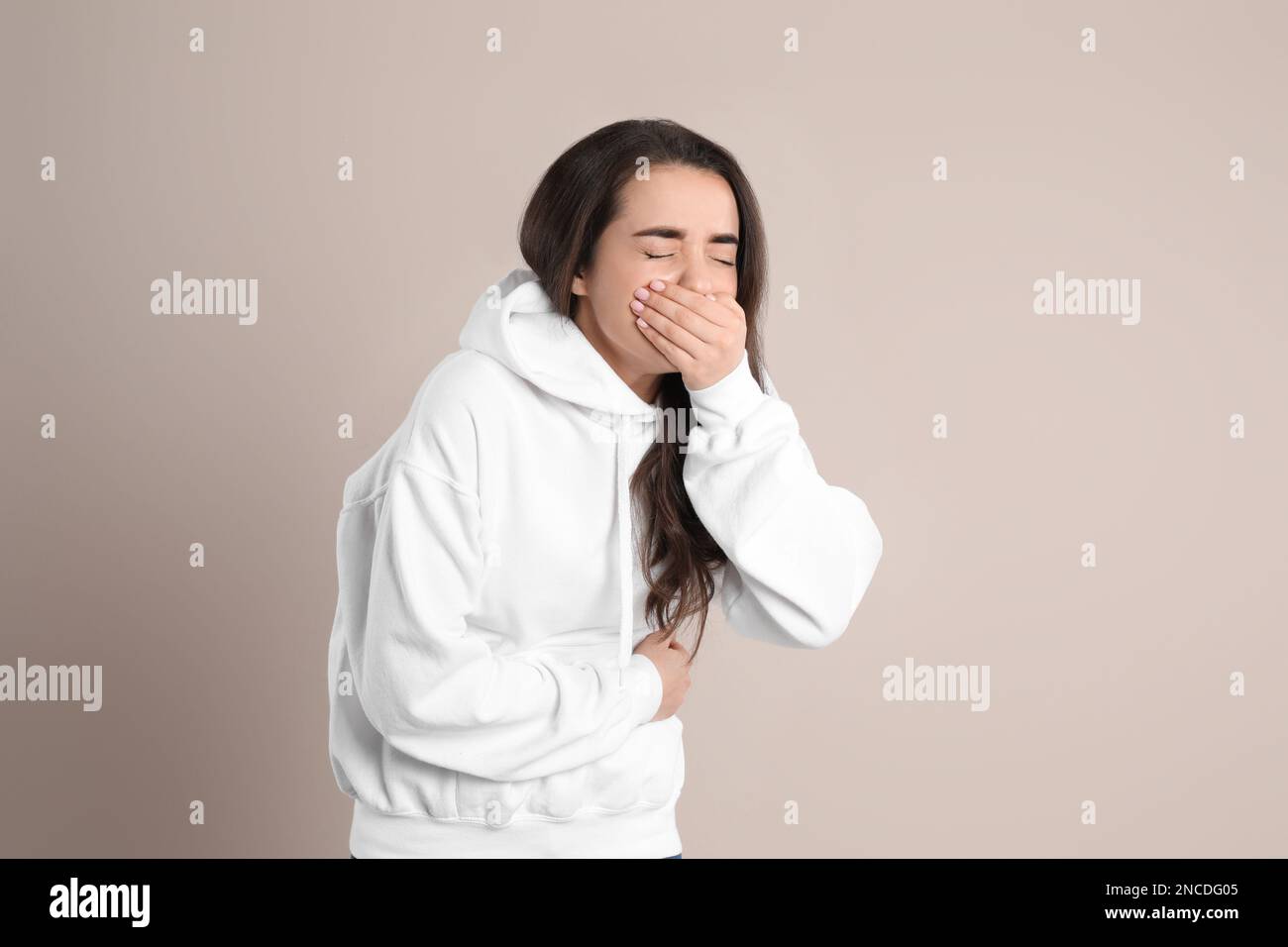 Young woman suffering from stomach ache and nausea on beige background