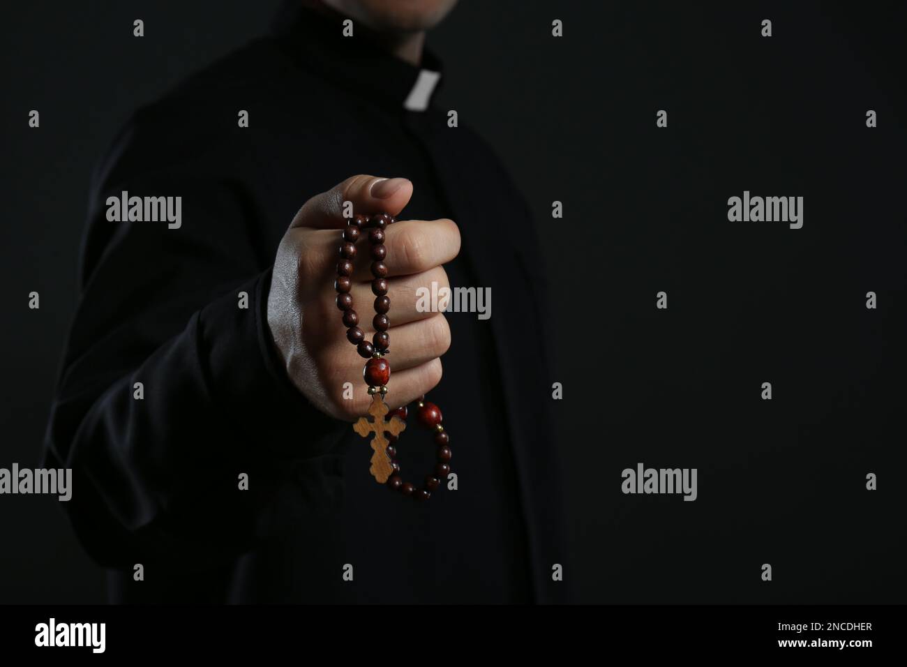 Priest with rosary beads on black background, closeup. Space for text Stock Photo