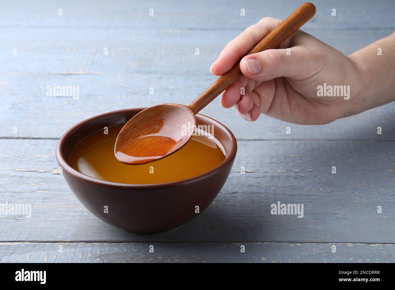 Woman with melted ghee butter at light grey wooden table, closeup Stock
