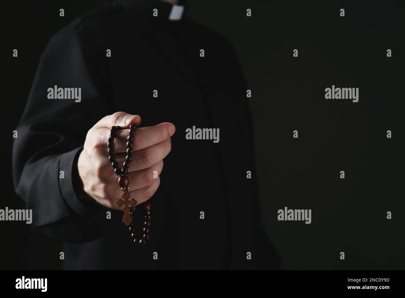 Priest with rosary beads on dark background, closeup. Space for text Stock Photo