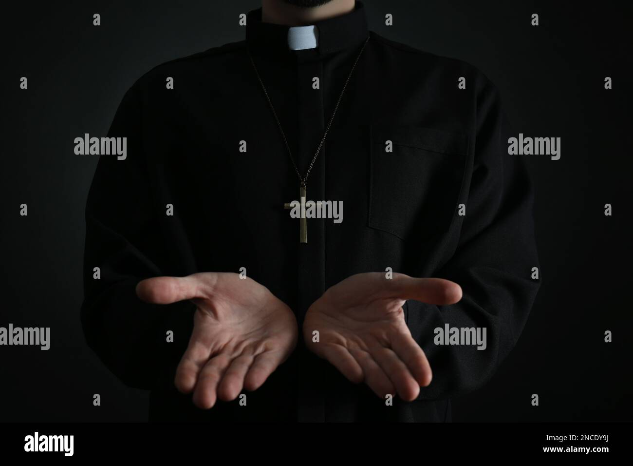 Priest reaching out his hands on dark background, closeup Stock Photo