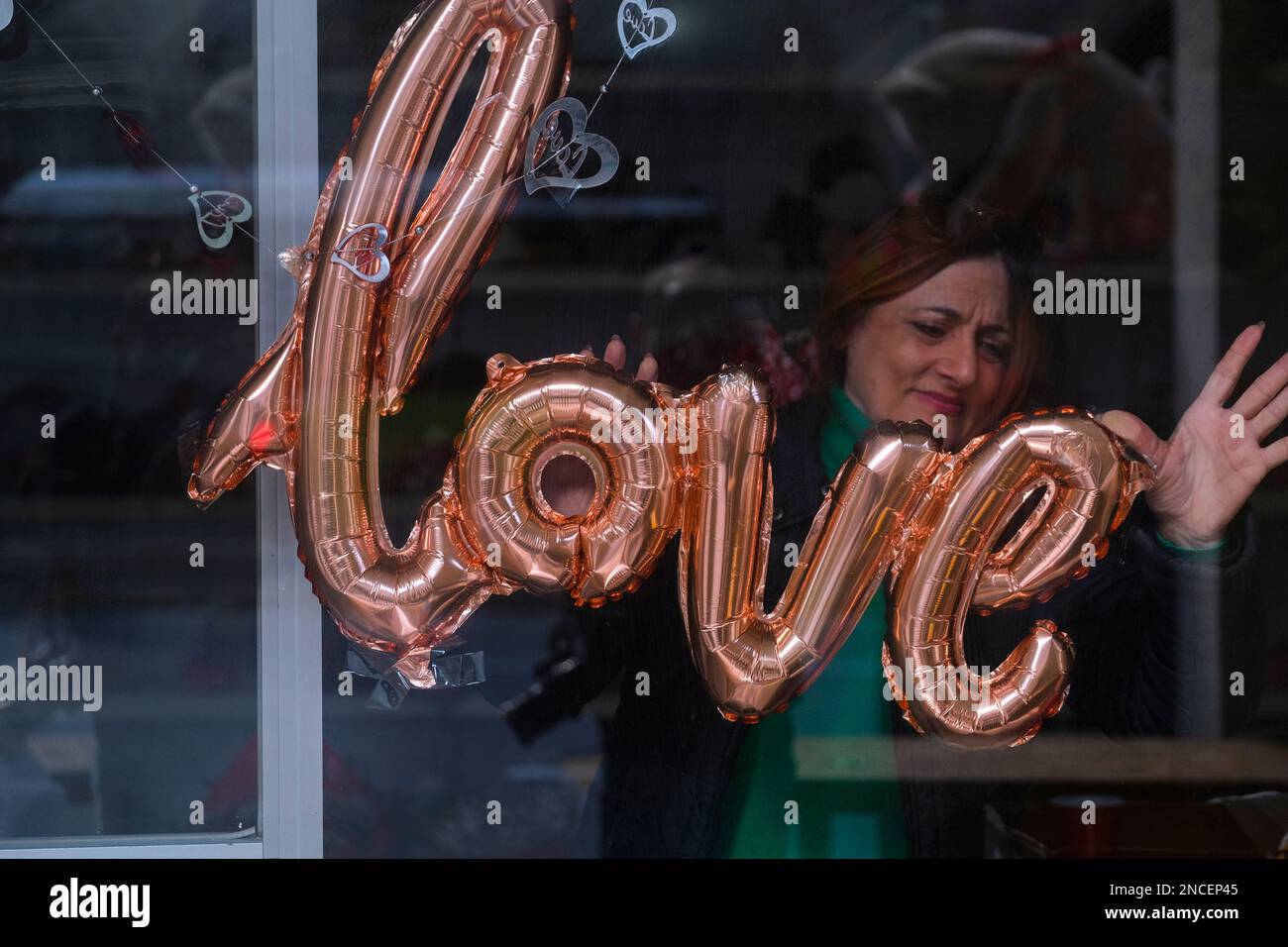 Valletta, Malta. 14th Feb, 2023. A woman sticks a foil balloon that resembles the word 'love' to a shop window on the occasion of Valentine's Day in Floriana, Malta, on Feb. 14, 2023. Credit: Jonathan Borg/Xinhua/Alamy Live News Stock Photo