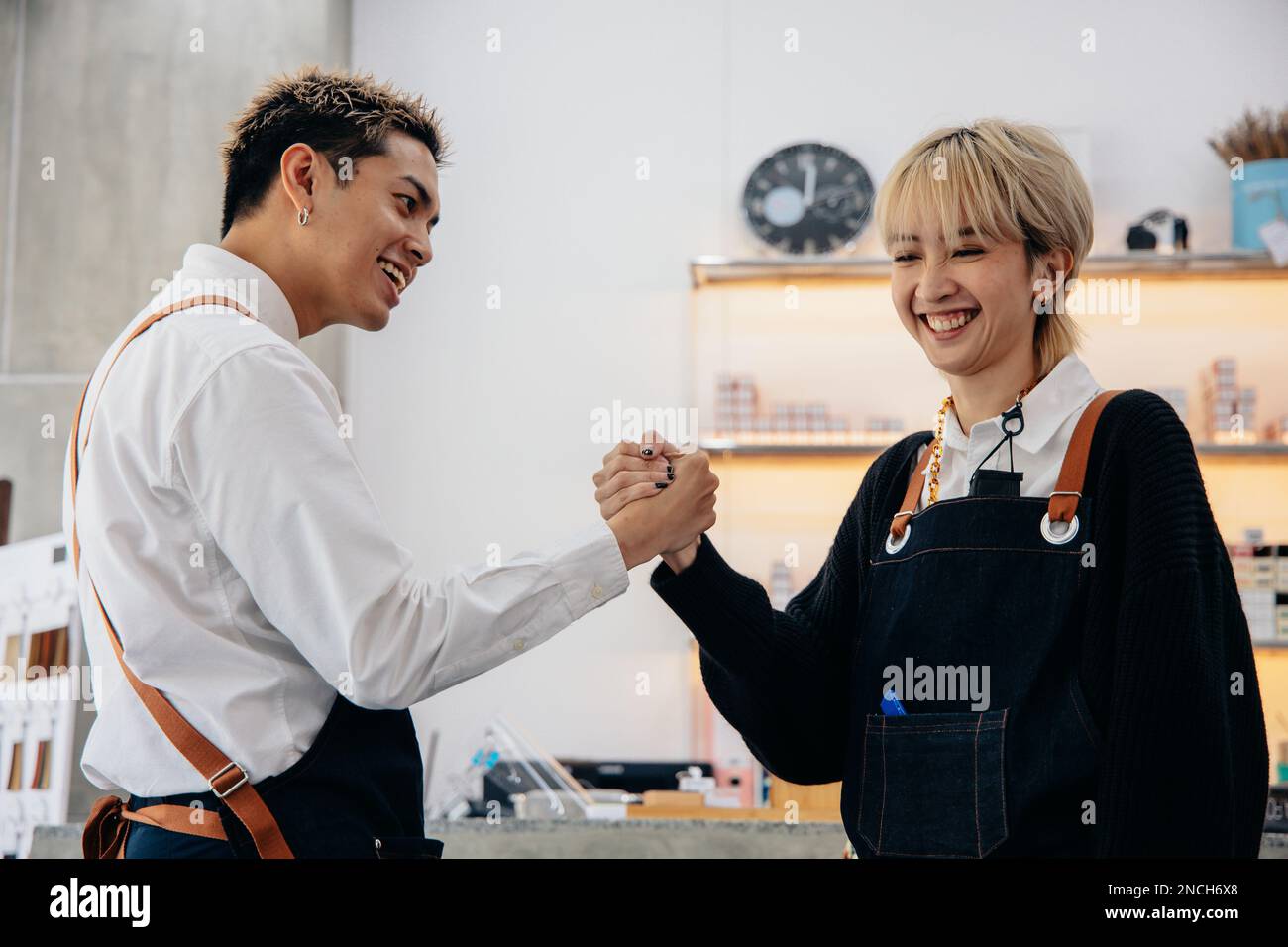 Cheerful young Asian man and woman hairdresser wearing apron uniform in modern salon giving high-five to each other on celebrating success of salon Stock Photo