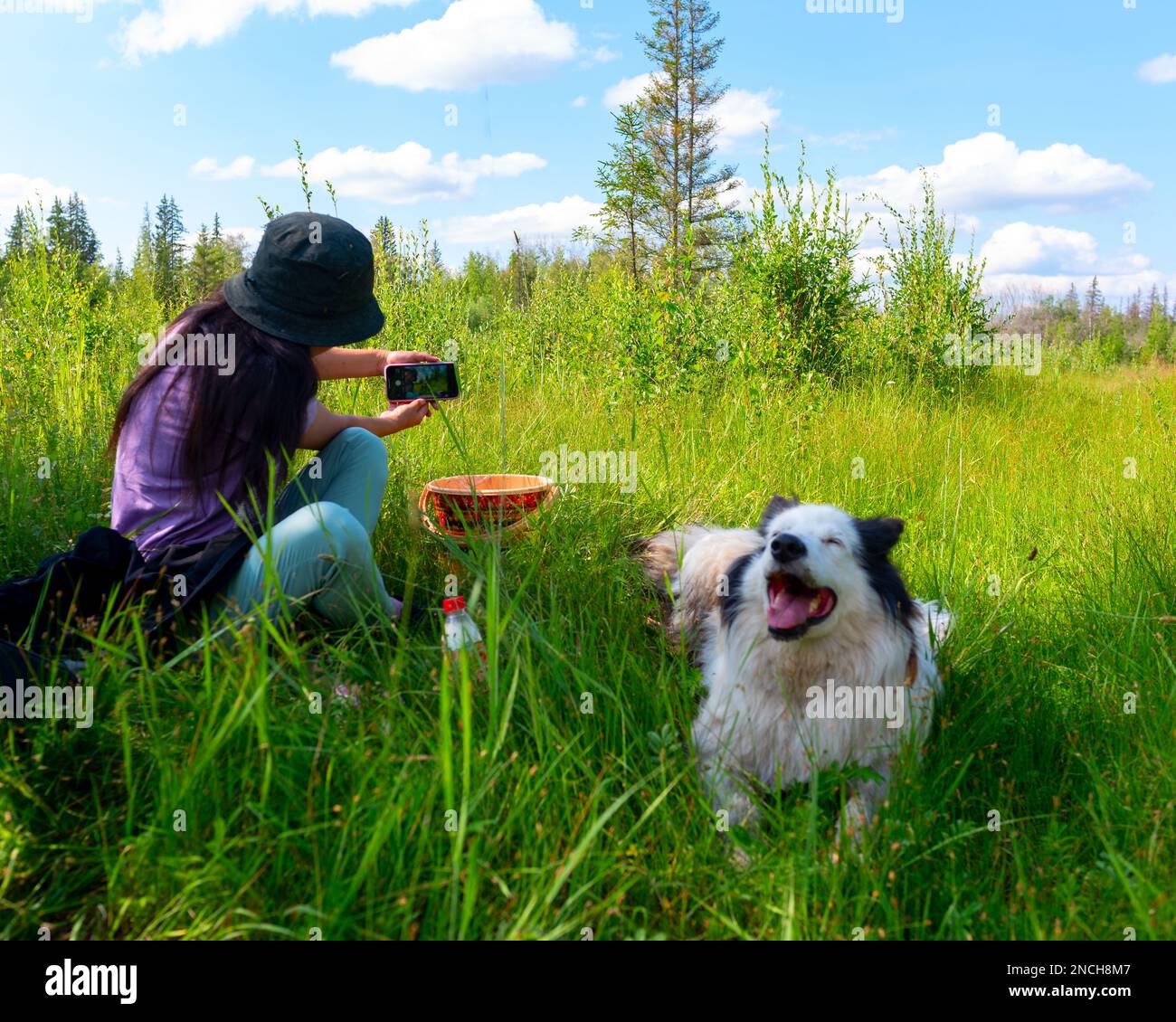 A girl in a hat sitting on the green grass makes a selfie on the phone ...