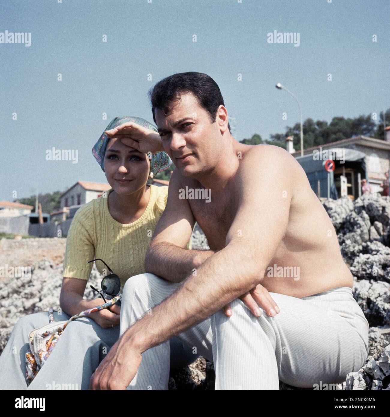 American actor Tony Curtis with his wife Christine Kaufmann sitting on rocks on the beach at