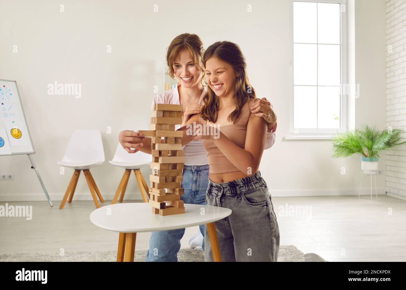 Laughing woman psychologist is playing tumbling tower with teen girl on therapy session. Stock Photo