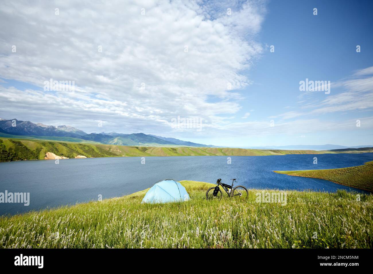 Mountain bike with tourist bags near blue tent camping at green hill near lake at mountain valley in Kazakhstan. Extreme Sport  bicycle bikepacking an Stock Photo