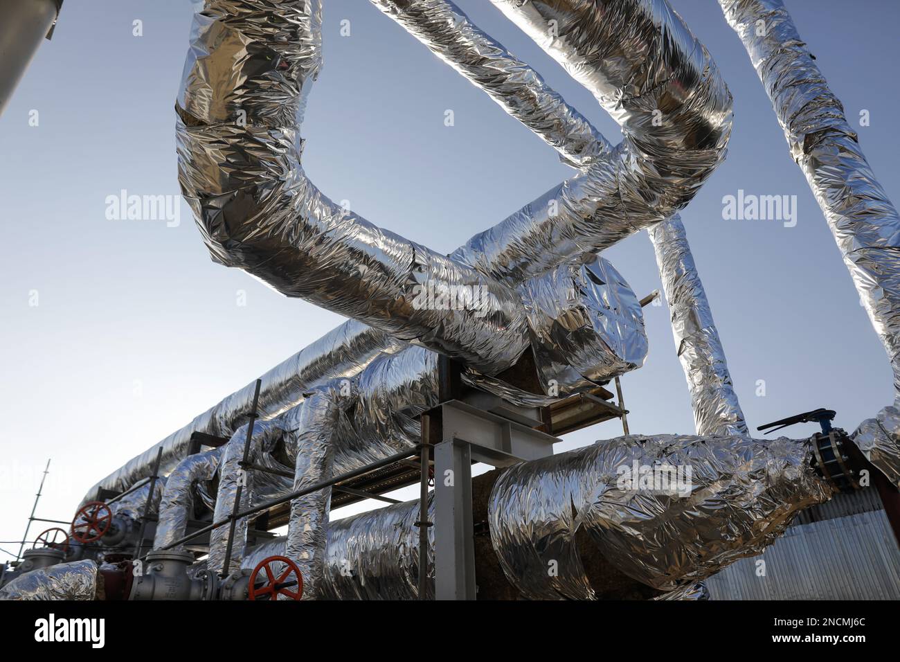Details with industrial metallic pipelines covered in tin foil through which hot water flows. Stock Photo