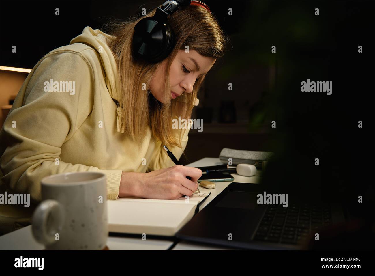 Focused woman in casual clothes wearing headphones looking at laptop ...