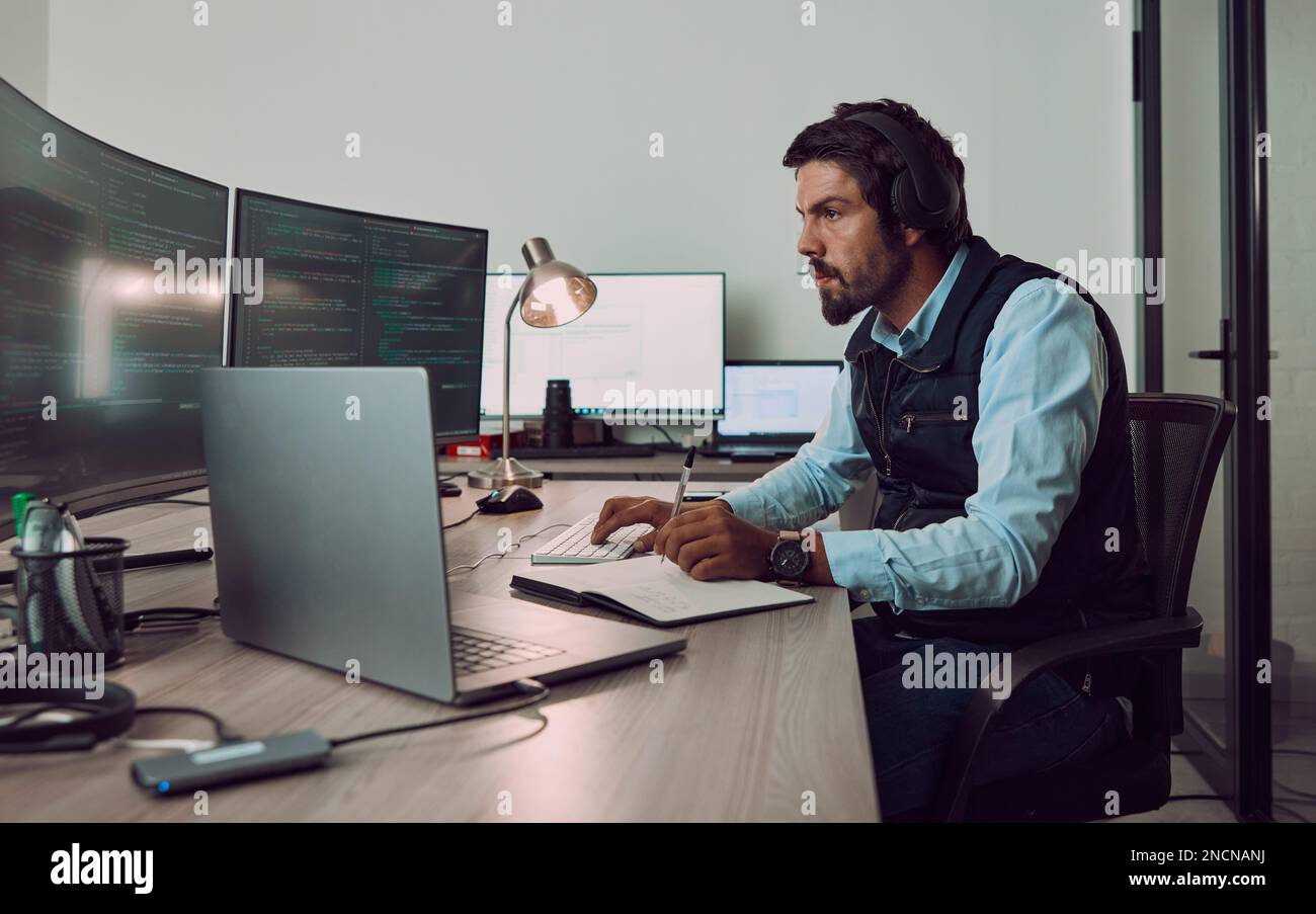Headphones, programmer and man on computer with book, coding or programming while writing notes at night. Information technology, notebook and male Stock Photo