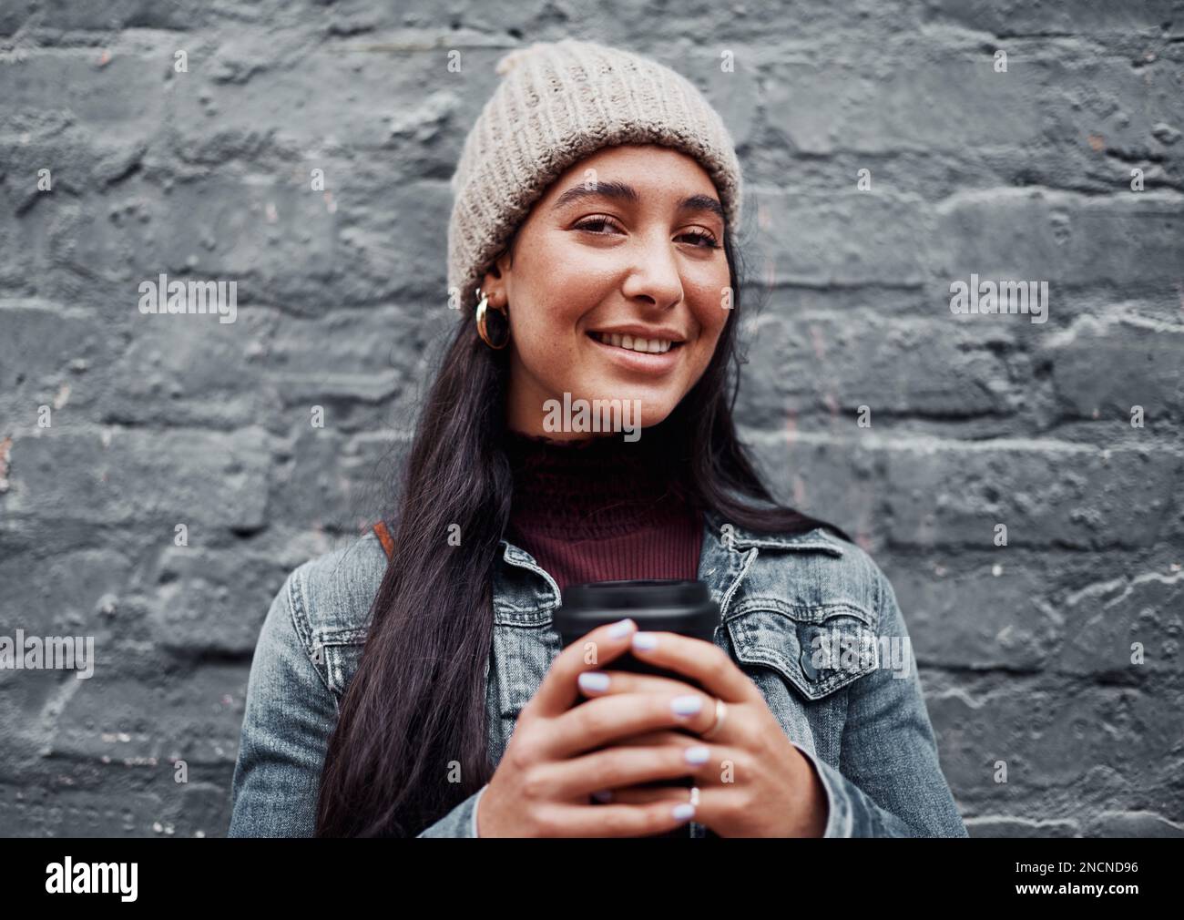 Just a typical city girl. Cropped portrait of an attractive teenage girl standing against a gray wall in the city and holding a coffee. Stock Photo