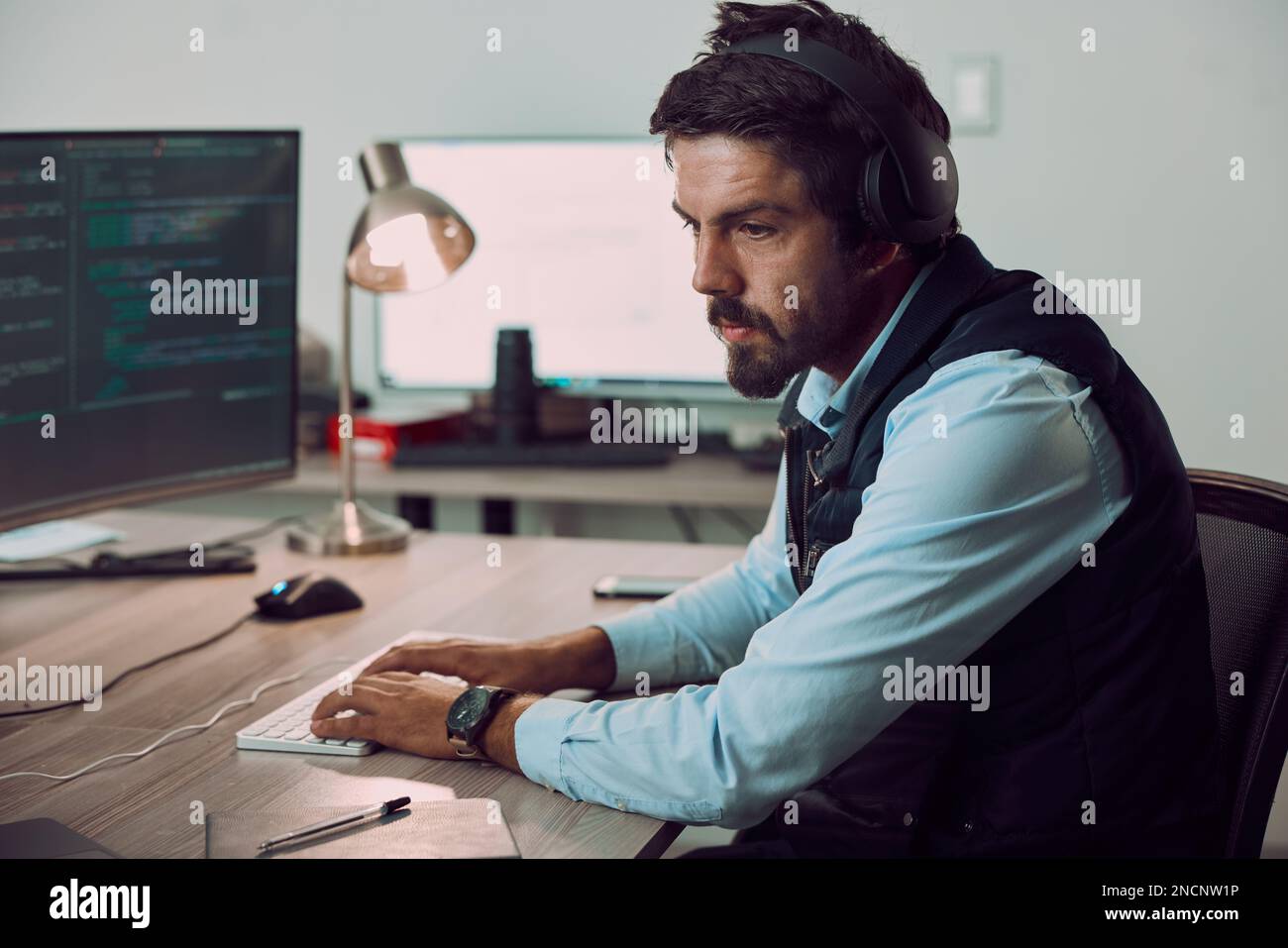 Headphones, programmer and man typing on computer, coding or programming at night. Information technology, thinking and male developer or coder Stock Photo