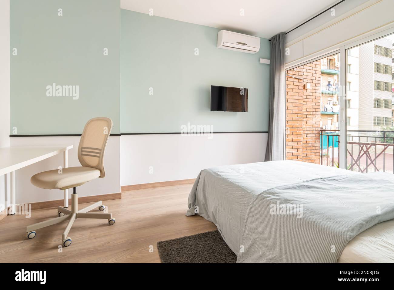 Spacious bright room with bed, large opening on entire wall with sliding plastic doors and access to balcony. Room has table with chair, air Stock Photo