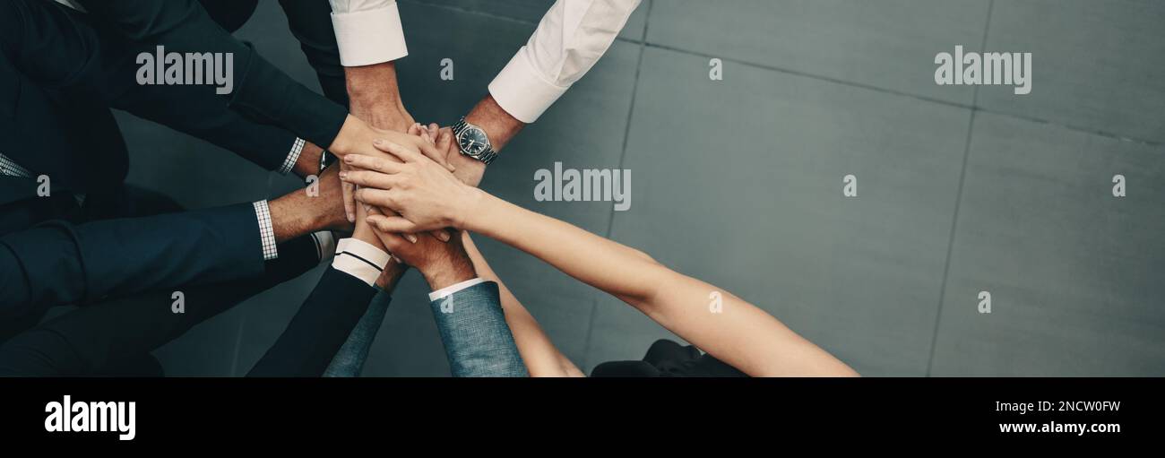Diverse group of business people coming together in a corporate huddle, stacking their hands together as they stand in an office. Team of professional Stock Photo